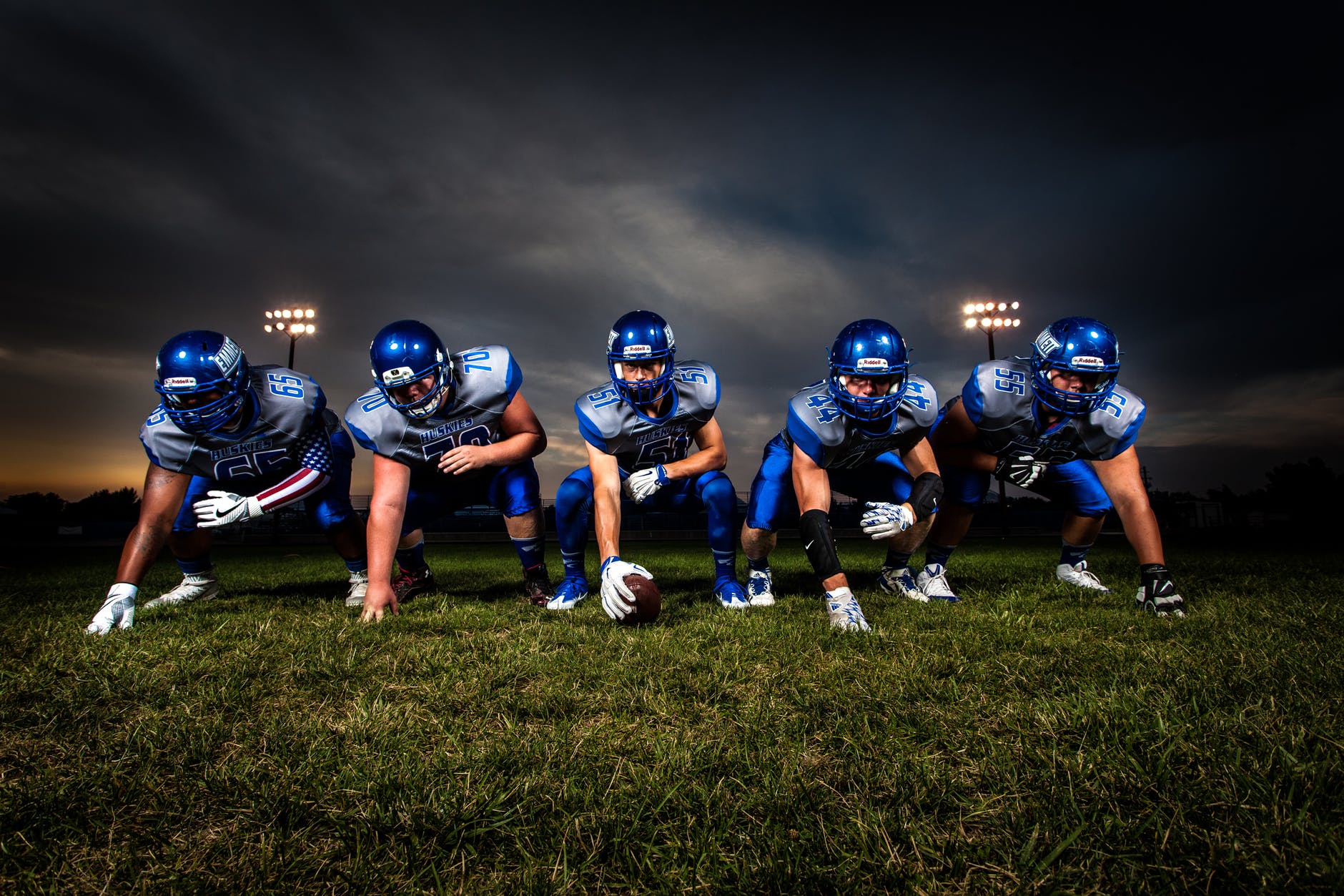 football players in blue jersey lined under grey white cloudy sky during sunset